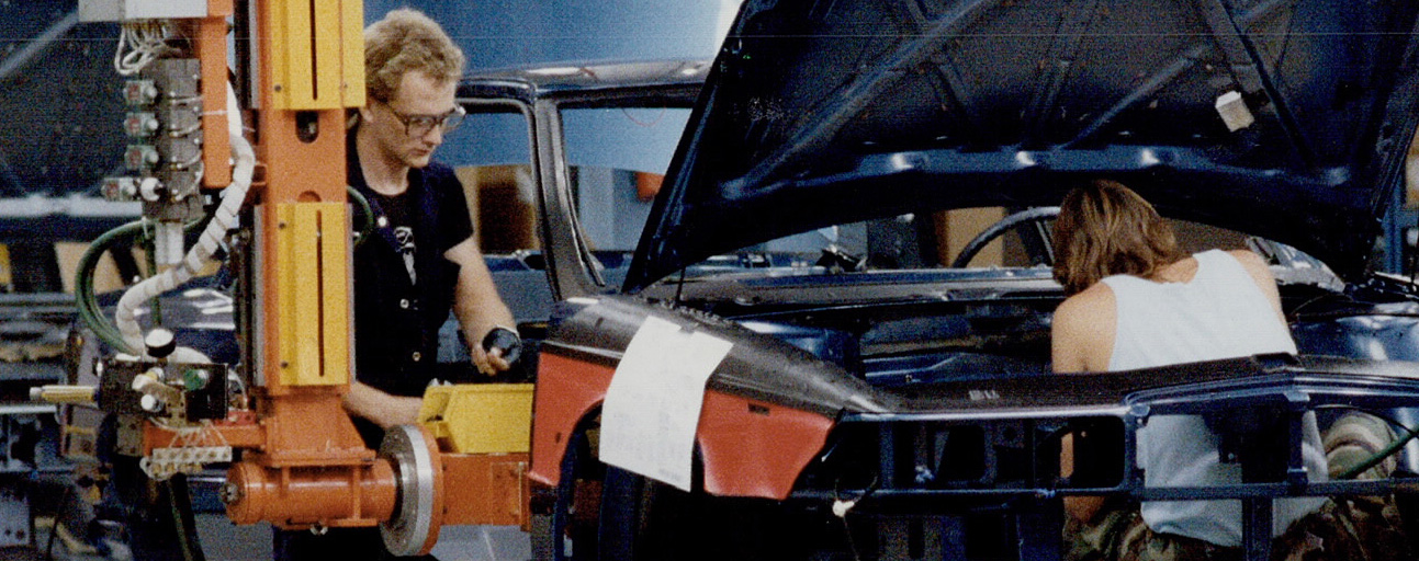 Image en couleur représentant trois hommes utilisant des machines-outils pour assembler une voiture sur une chaîne de montage.