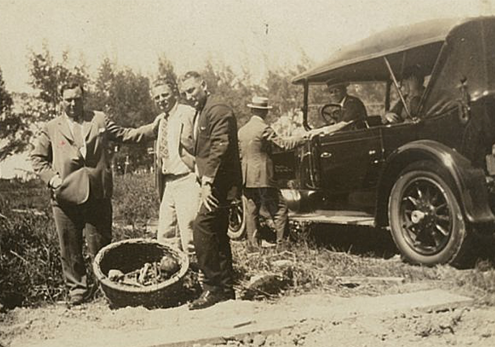 Trois hommes prennent la pose devant une automobile de l'époque.