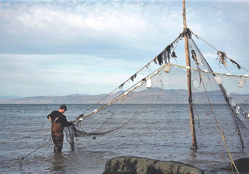 Un homme portant des bottes-pantalon est debout dans l'eau du fleuve et tient la base d'un filet de pêche attaché au sommet d’un poteau de 6 m de haut.