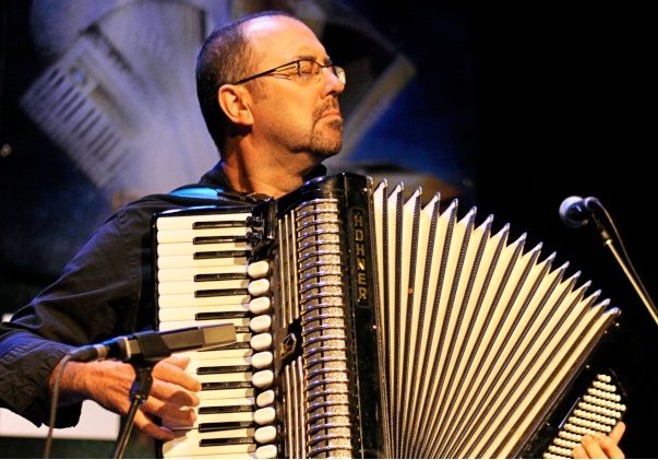 Photographie couleur où Martin Bellemare debout avec un accordéon-piano, les yeux fermés, joue face au public