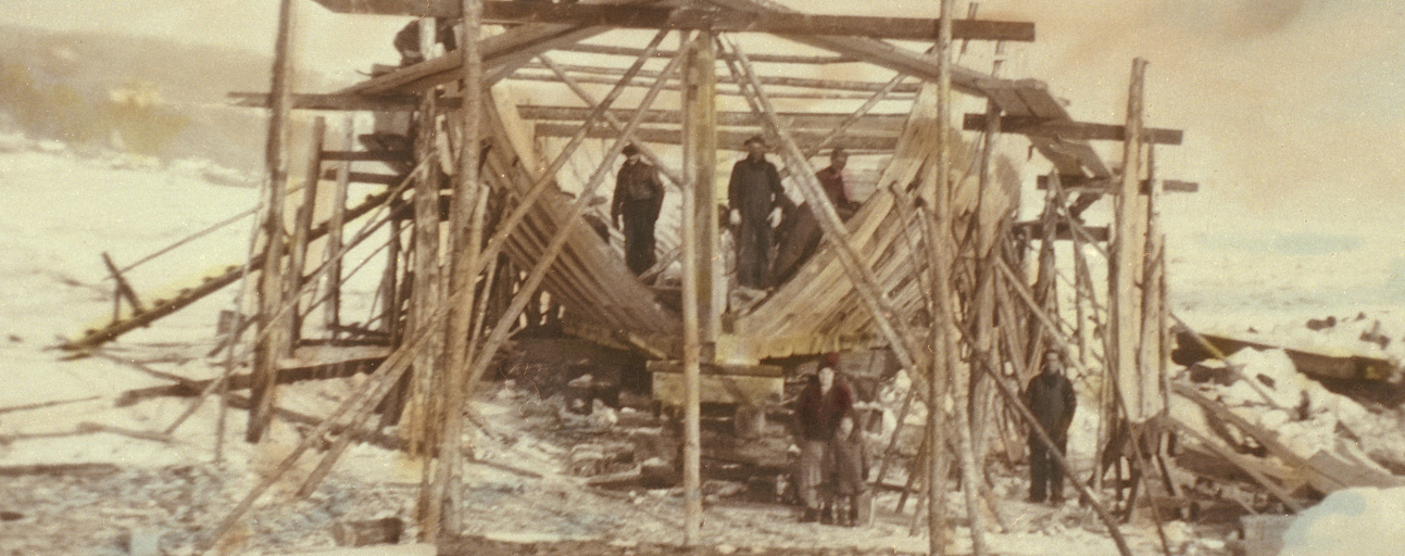 Vue d'une goélette en construction. On y voit la charpente du bateau entourée par des échafaudages.