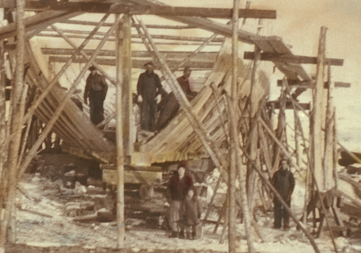 Vue d'une goélette en construction. On y voit la charpente du bateau entourée par des échafaudages.