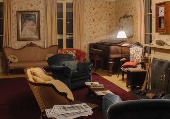 Salon de la résidence d'été avec deux canapés, deux fauteuils, un piano et un foyer.