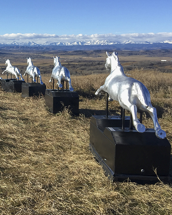 Photo couleur d’un paysage avec huit chevaux mécaniques à pièces alignés devant le panorama de la montagne