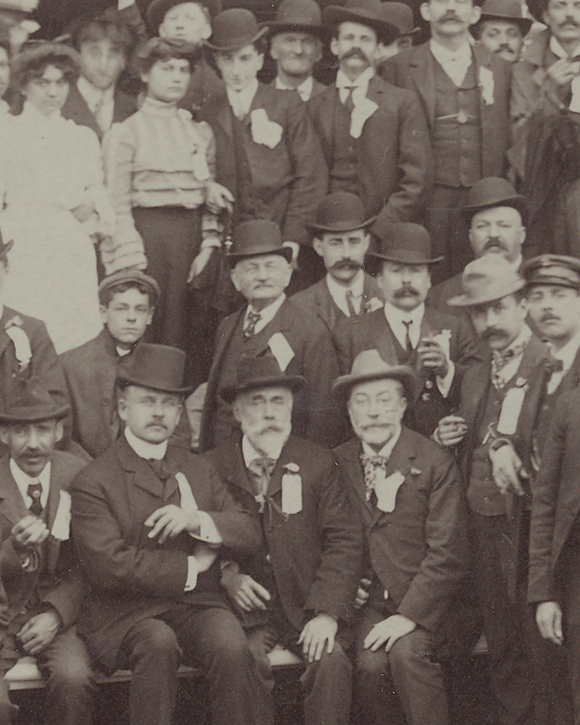 Photographie sépia illustrant des hommes et quelques femmes à l’extérieur devant une usine.