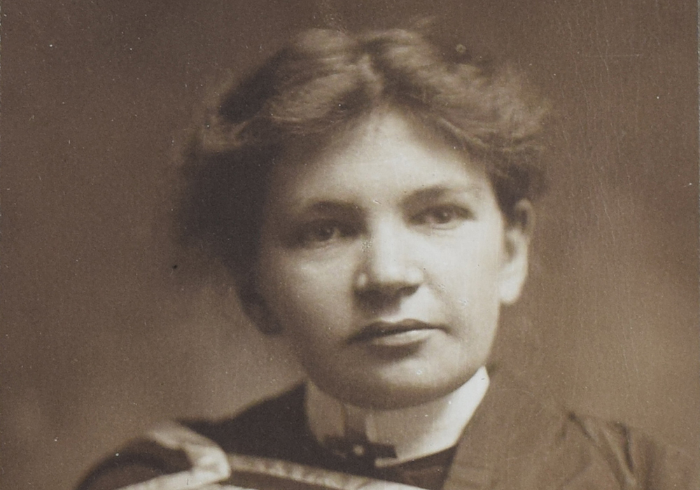 Photographie en noir et blanc de Maude Abbott, jeune adulte, de la taille à la tête. Elle porte un habit et une toge de graduation. Ses cheveux foncés sont attachés à l’arrière de sa tête et sa tête est légèrement tournée vers la gauche.