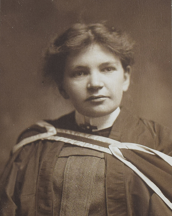 Photographie en noir et blanc de Maude Abbott, jeune adulte, de la taille à la tête. Elle porte un habit et une toge de graduation. Ses cheveux foncés sont attachés à l’arrière de sa tête et sa tête est légèrement tournée vers la gauche.