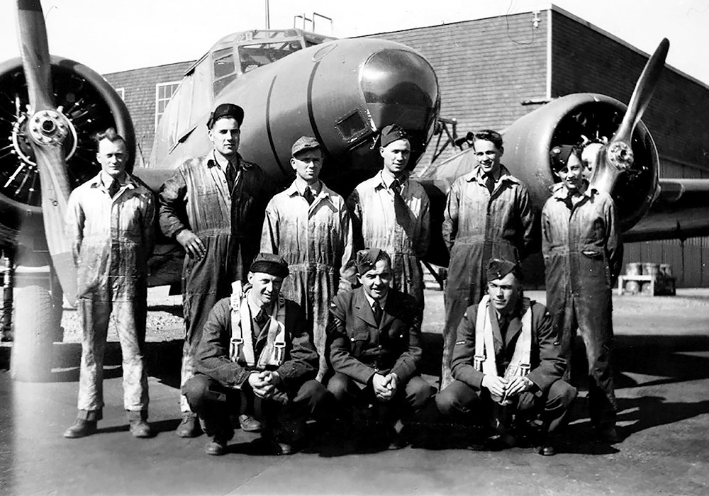 3 aviateurs et 6 mécaniciens devant un avion et un hangar.