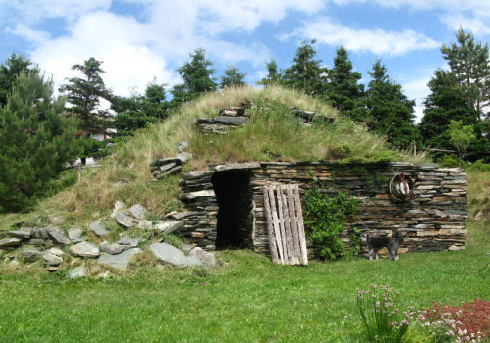 Extérieur d’une cave à légumes à flanc de colline, avec façade en pierres empilées et dessus recouvert d’herbe.