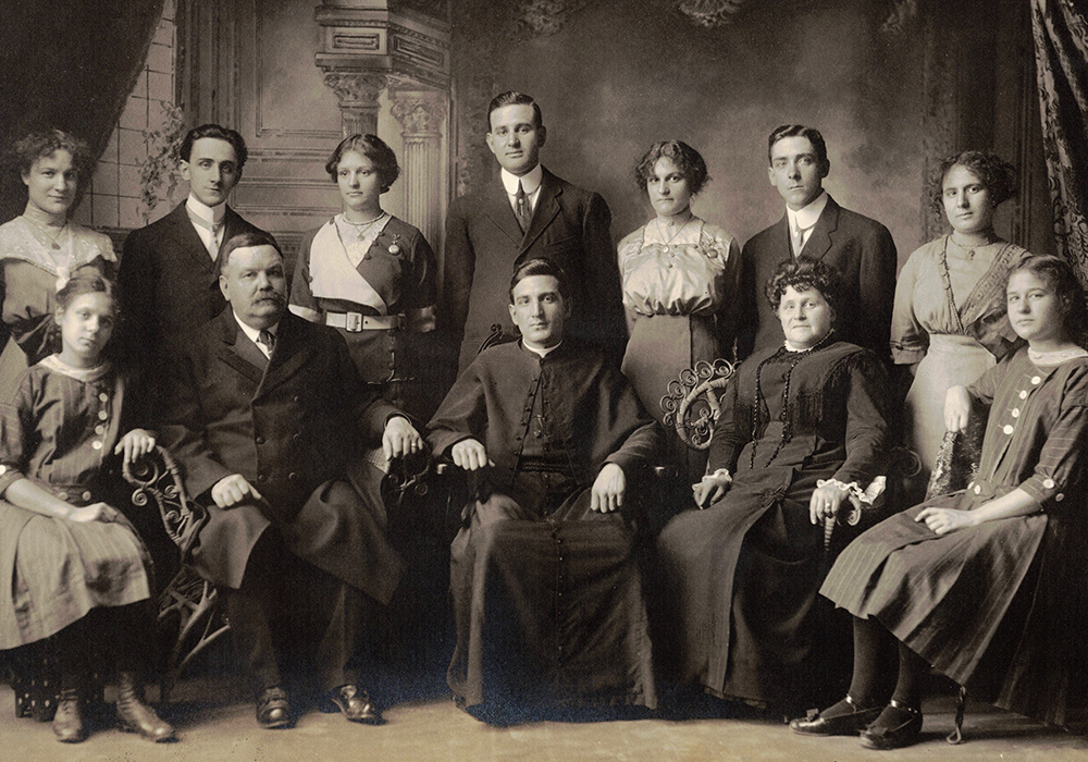 Photographie noir et blanc prise en studio. 12 personnes dans leurs beaux habits du début du 20e siècle. À l’avant sont assis Monseigneur Alfred LePailleur, ses parents et ses 2 plus jeunes sœurs. Debout à l’arrière, sont les autres membres de la fratrie.