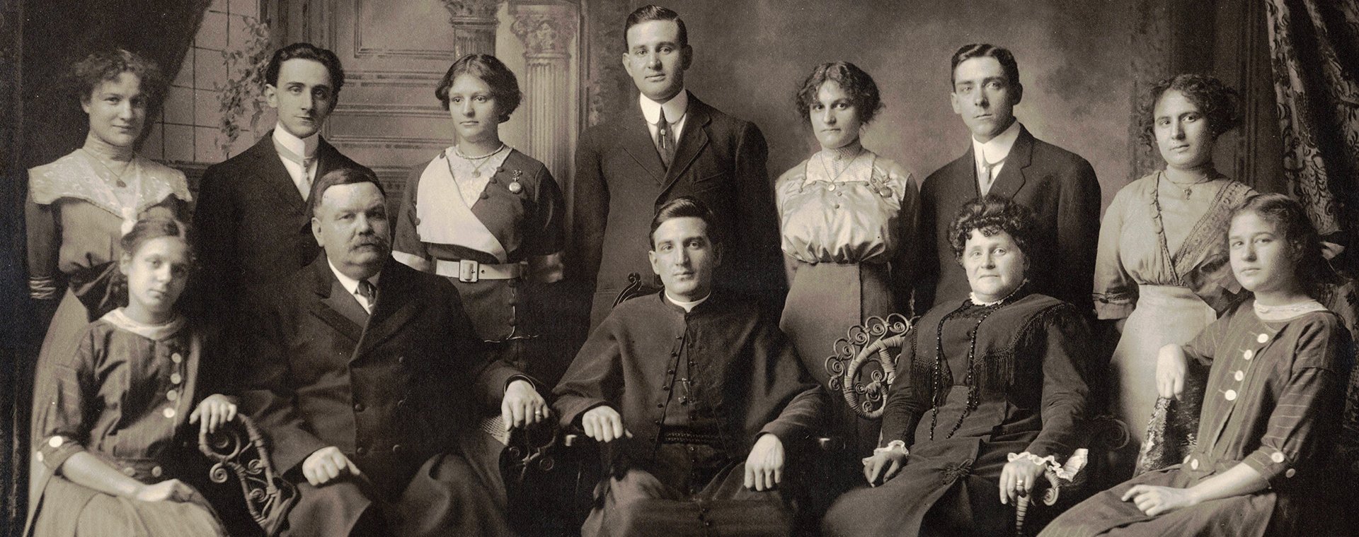Photographie noir et blanc prise en studio. 12 personnes dans leurs beaux habits du début du 20e siècle. À l’avant sont assis Monseigneur Alfred LePailleur, ses parents et ses 2 plus jeunes sœurs. Debout à l’arrière, sont les autres membres de la fratrie.
