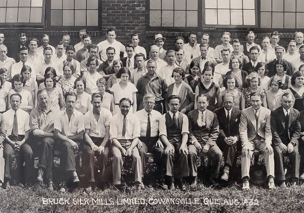 Black and white panoramic photo. A large number of employees and managers of the company pose in front of the factory on four rows.