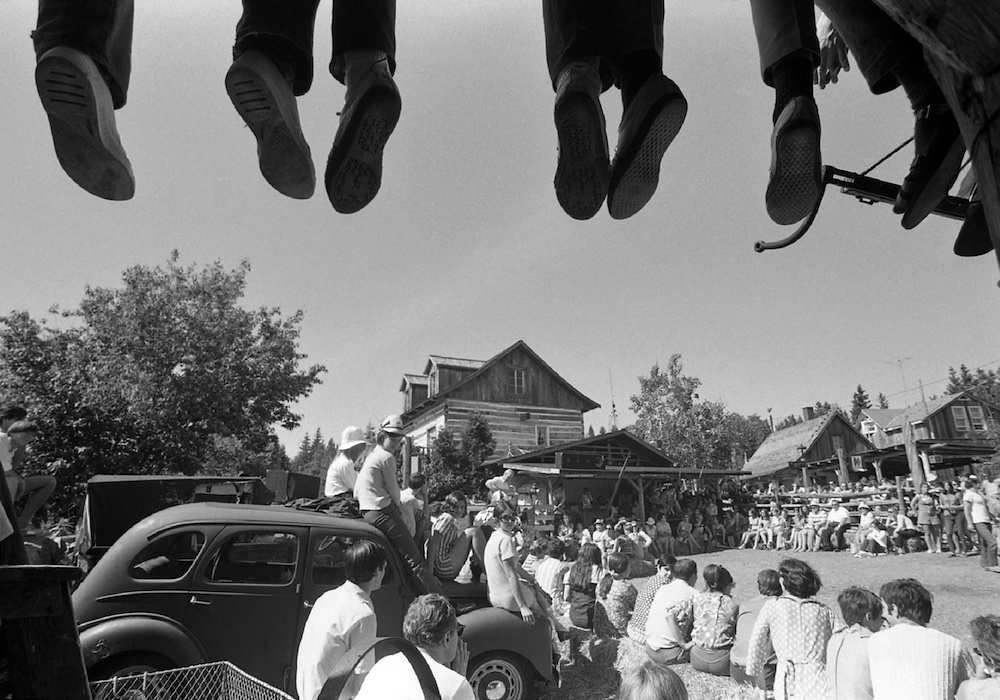 Photo noir et blanc d’une centaine de spectateurs assistant à une prestation extérieure à La Butte. Le haut de l’image montre les pieds de personnes installées sur une partie de la toiture de la Butte.