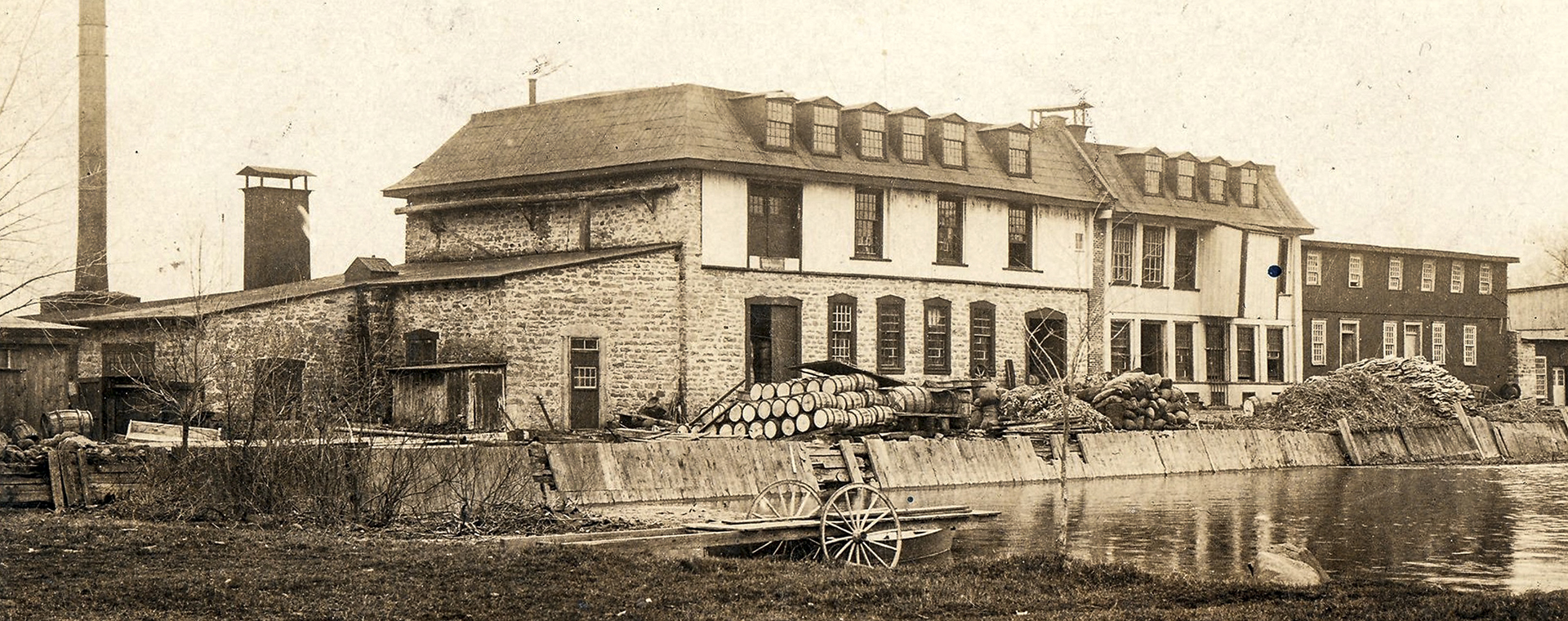 Carte postale publiée vers 1900. Au centre : la fabrique de papier avec, à sa gauche, sa haute cheminée sur la digue des moulins encombrée de tonneaux et de matériaux. À l'avant-plan: un quai roulant donne sur le bassin d’eau.