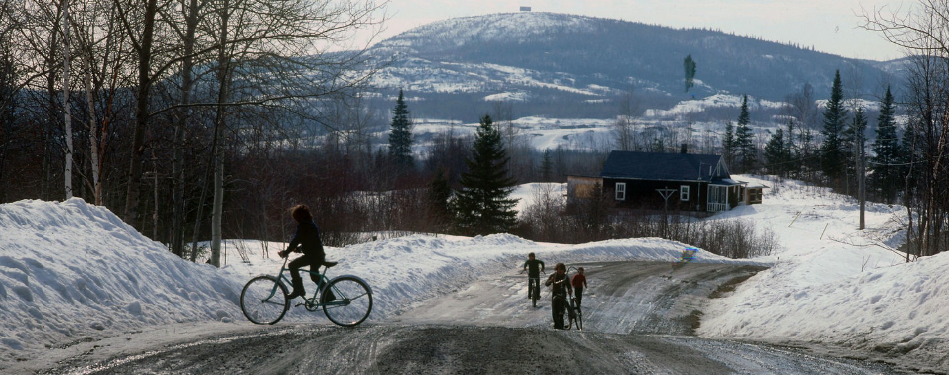 Vue d'un paysage et d'une route rurale au printemps durant la fonte des neiges. Des enfants circulent à vélo.