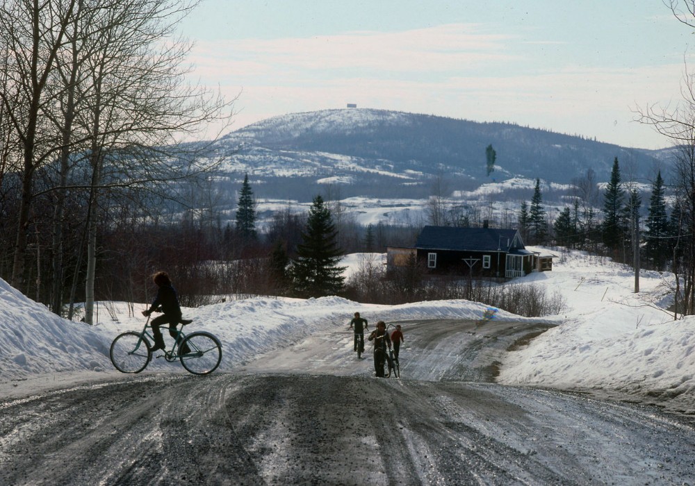 Vue d'un paysage et d'une route rurale au printemps durant la fonte des neiges. Des enfants circulent à vélo.