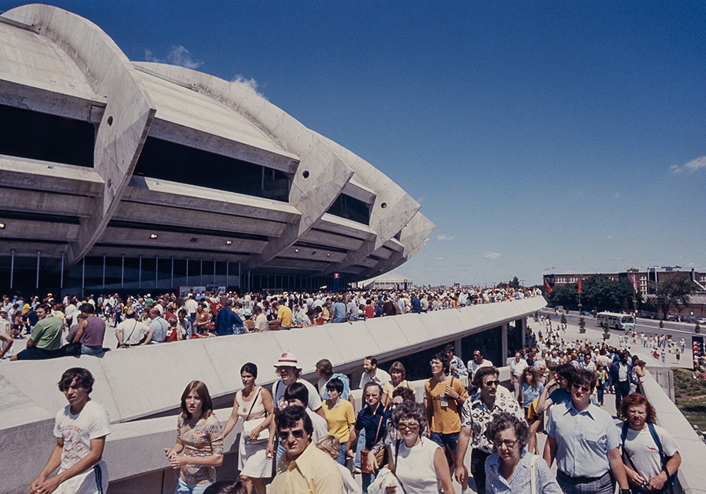 De nombreuses personnes vêtues d’habits d’été colorés se dirigent vers le Stade olympique, en empruntant une large rampe de béton. D’autres sont assises sur le rebord de l’esplanade bondée entourant le bâtiment.